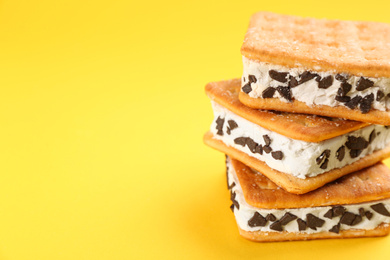 Sweet delicious ice cream cookie sandwiches on yellow background, closeup. Space for text
