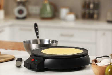 Photo of Cooking delicious crepe on electric pancake maker on white marble table in kitchen, space for text
