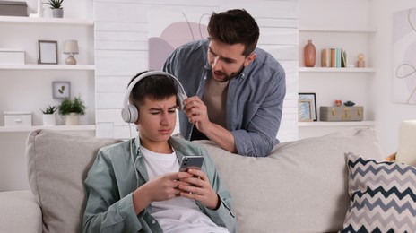 Father scolding his son while he listening music in headphones at home. Teenager problems