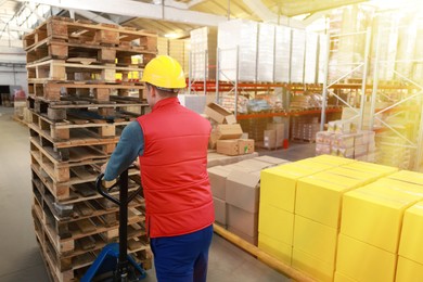 Worker moving wooden pallets with manual forklift in warehouse, back view
