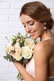 Photo of Young bride with elegant hairstyle holding wedding bouquet near white brick wall