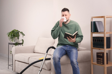 Man with book suffering from dust allergy at home