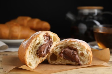 Tasty croissant with chocolate and sugar powder on wooden table. Space for text