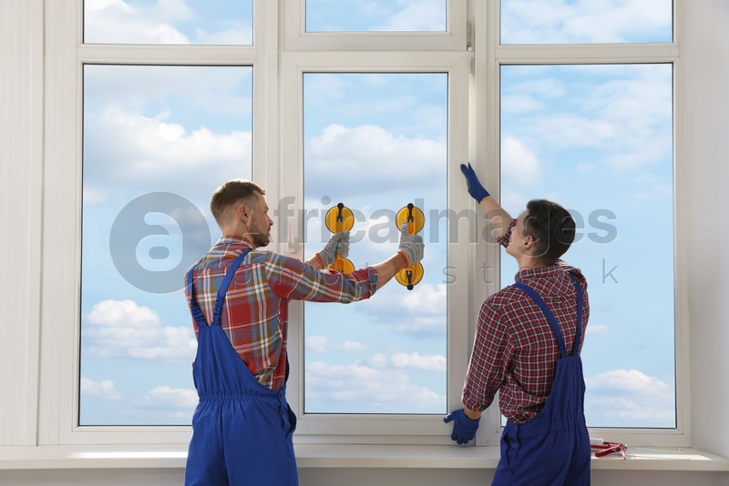 Workers using suction lifters during plastic window installation indoors