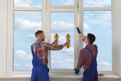 Workers using suction lifters during plastic window installation indoors