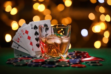 Casino chips, cards and alcohol drink on green table against blurred lights. Straight poker combination