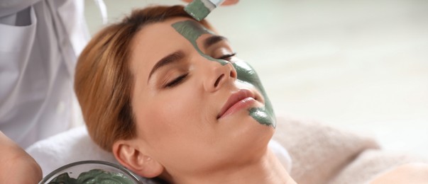 Cosmetologist applying mask onto woman's face in spa salon. Banner design