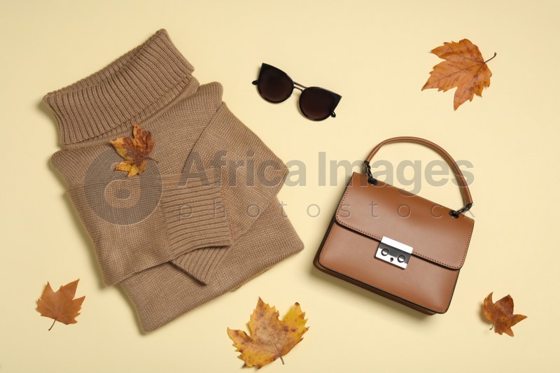 Photo of Sweater, bag and sunglasses with dry leaves on yellow background, flat lay. Autumn season