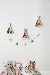 Wigwam shaped shelves, stuffed toys and garland indoors. Children's room interior design