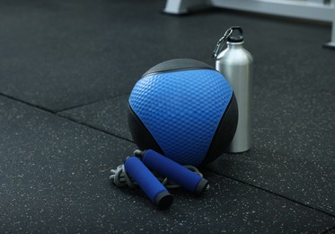 Blue medicine ball, bottle and skipping rope on floor in gym, space for text