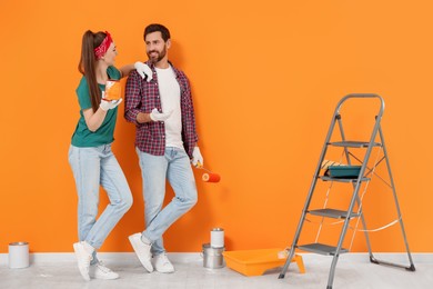 Photo of Happy designers with painting equipment near freshly painted orange wall indoors