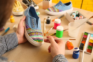 Man painting on sneaker at table, closeup. Customized shoes
