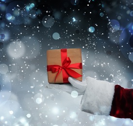 Santa Claus holding gift box on winter background, bokeh effect