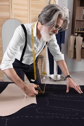 Professional tailor cutting fabric by following chalked sewing pattern at table in workshop