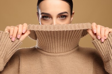 Photo of Portrait of beautiful young woman in stylish sweater on light brown background, closeup