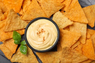 Delicious nachos and cheese sauce with basil on board, top view