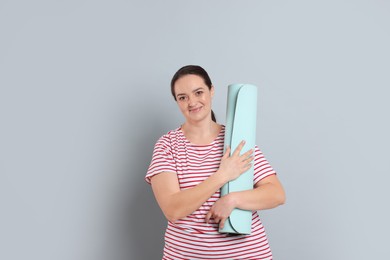 Happy overweight woman with yoga mat on grey background