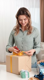 Beautiful young woman wrapping gift at table indoors