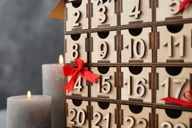 Wooden Christmas advent calendar and burning candles on grey background, closeup