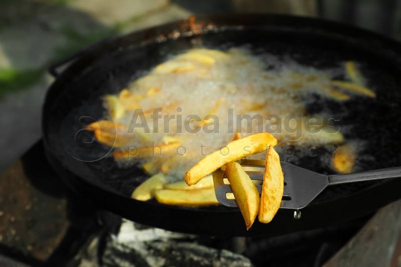 Cooking delicious potato wedges on frying pan outdoors