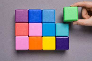 Photo of Woman holding wooden cube near others on grey background, top view. Management concept
