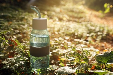 Photo of Glass bottle of water in green grass on sunny day. Space for text