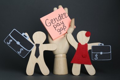 Photo of Gender pay gap. Wooden mannequin hand with paper note, figures of man and woman on black background