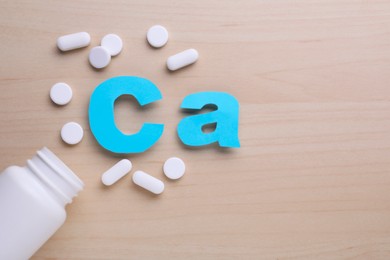 Photo of Paper symbol Ca (Calcium), medical bottle and pills on violet background, top view