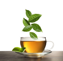 Image of Green leaves falling into cup of tea on table against white background