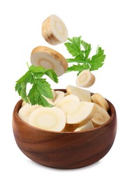 Image of Pieces of parsnip root and leaves falling into wooden bowl on white background