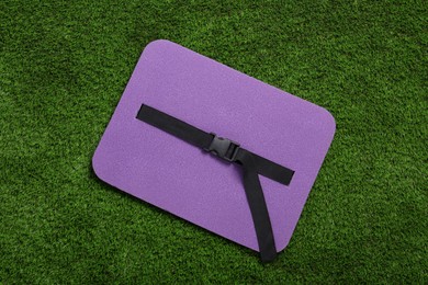 Violet foam seat mat for tourist on green grass, top view