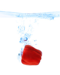 Red bell pepper falling down into clear water against white background