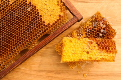 Photo of Fresh delicious honeycombs and hive frame on wooden table, flat lay