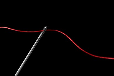 Sewing needle with red thread on black background