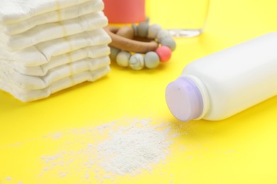 Photo of Bottle, scattered dusting powder and diapers on yellow background. Baby care products