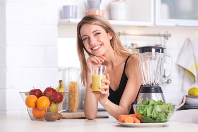 Young woman with glass of tasty healthy smoothie at table in kitchen