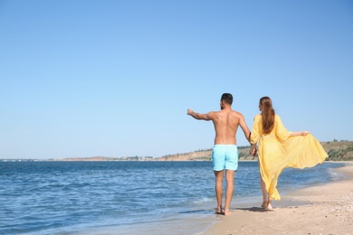 Woman in bikini and her boyfriend on beach, back view with space for text. Lovely couple