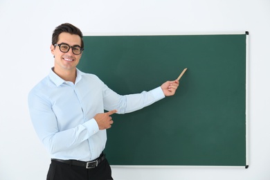 Young teacher with ruler near blank chalkboard in classroom. Space for text