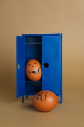Happy egg hiding in closet and playing prank on another one against brown background