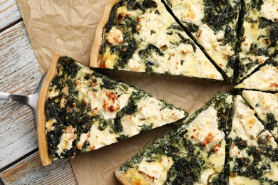Photo of Taking piece of delicious homemade spinach quiche on rustic wooden table, flat lay