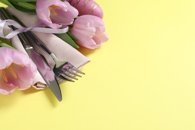 Photo of Cutlery set and tulips on pale yellow background, space for text. Easter table setting