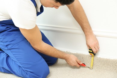Worker with cutter knife and measuring tape installing new carpet indoors, closeup
