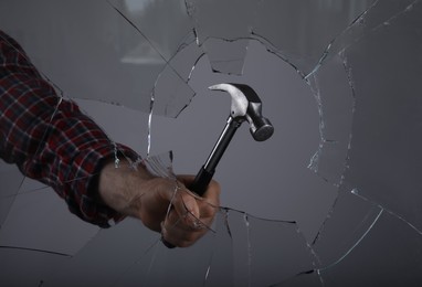 Man breaking window with hammer on grey background, closeup