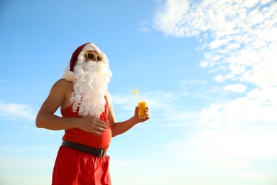 Santa Claus in beach outfit with cocktail outdoors, space for text. Christmas vacation