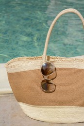 Stylish bag and sunglasses near outdoor swimming pool on sunny day. Beach accessories