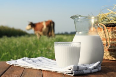 Photo of Milk with hay on wooden table and cow grazing in meadow