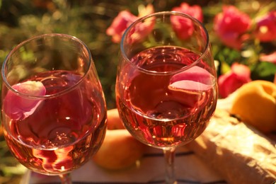 Photo of Glasses of delicious rose wine with petals outside, closeup