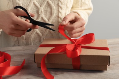 Photo of Woman decorating gift box at wooden table, closeup. Christmas present