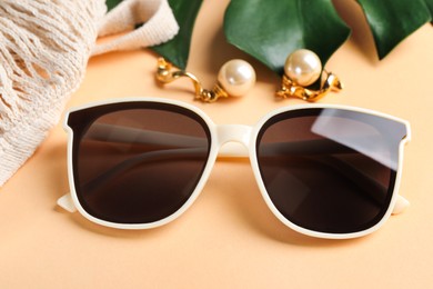 New stylish elegant sunglasses and beautiful earrings on beige background, closeup