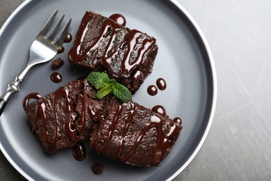 Photo of Delicious chocolate brownies with sweet syrup and mint served on grey table, top view